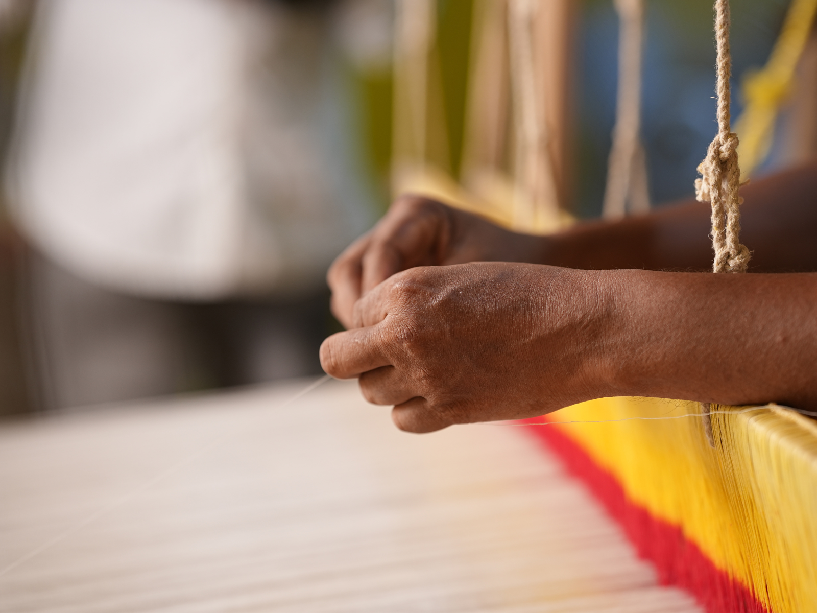 An artisan’s hands at the loom, weaving red and yellow thread in a village craft studio
