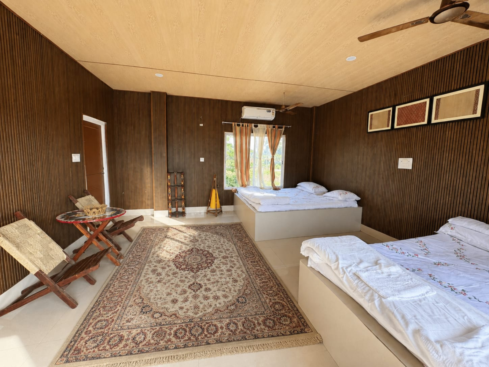 Super Deluxe Room with two king size beds, wood-panelled walls, cane folding chairs and a painted table