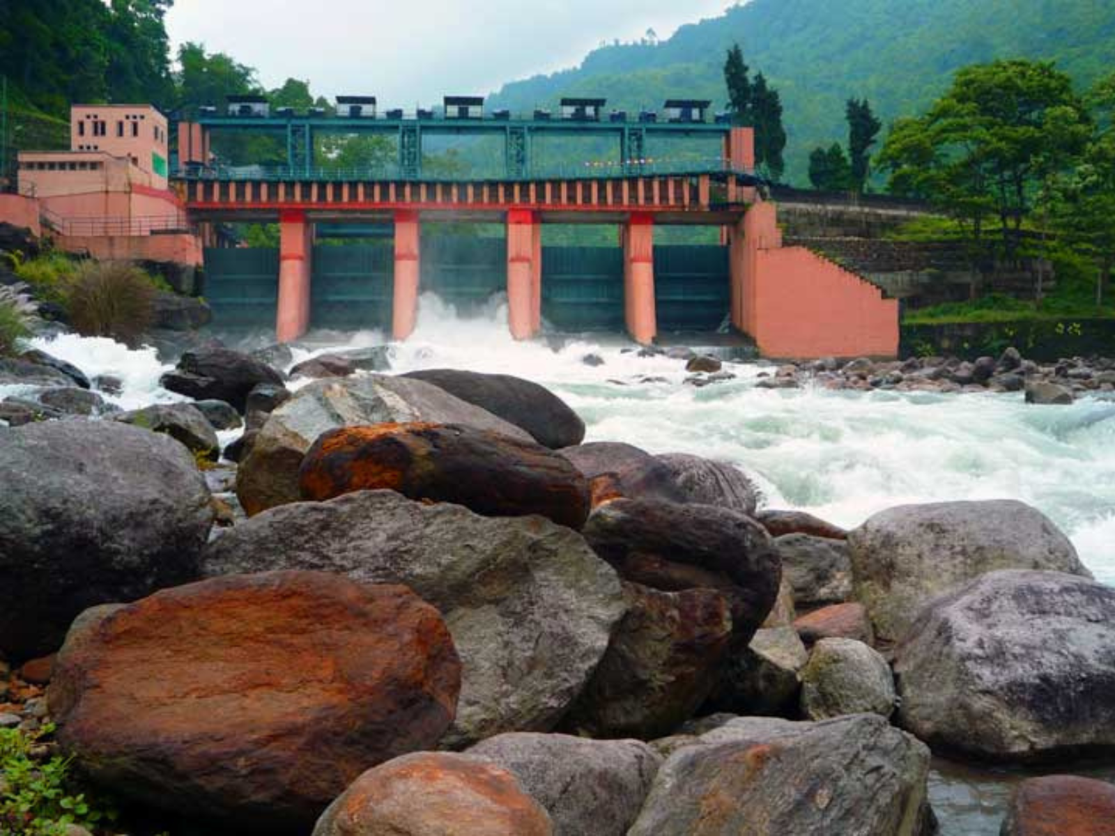 The Jaldhaka barrage with white water rushing over boulders below the green hills