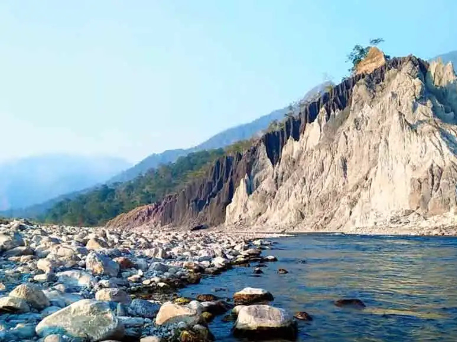 Pale eroded cliffs above a boulder-strewn riverbed and clear water near Narathali